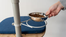A hand placing a food bowl into a holder on the Freestyle cat tree pole