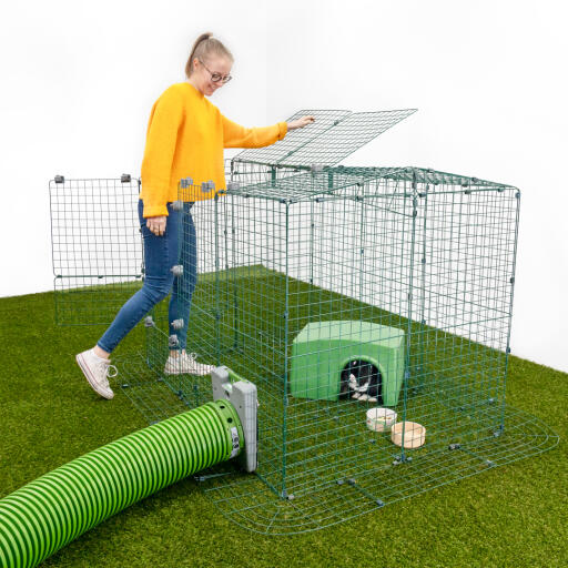 A girl opening a section of an animal run with rabbits inside in a shelter with a Zippi run