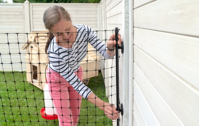 Woman attaching Omlet Chicken Fencing to a wooden wall in garden